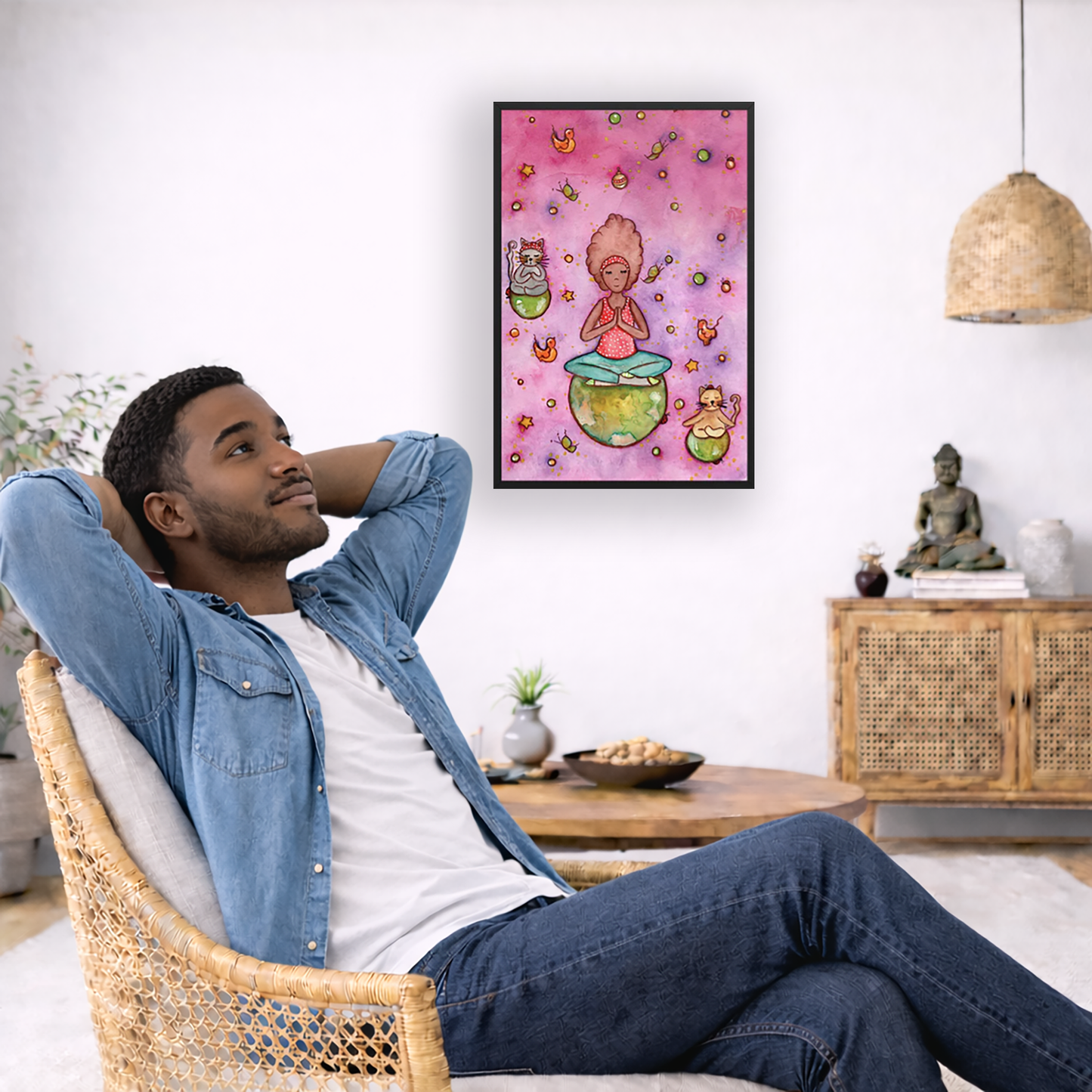 Poster of a woman and her cats meditating atop their own personal worlds with a pink background. The poster is framed and is in the center of the living room wall. To the left a man is relaxing in her chair with his hands behind his head. There is a small coffee table beside him with a bowl of walnuts, incense and a small green plant. On the right side of the room is a cabinet with a Buddha statue, books and an urn on it. To the left is a green floor plant.