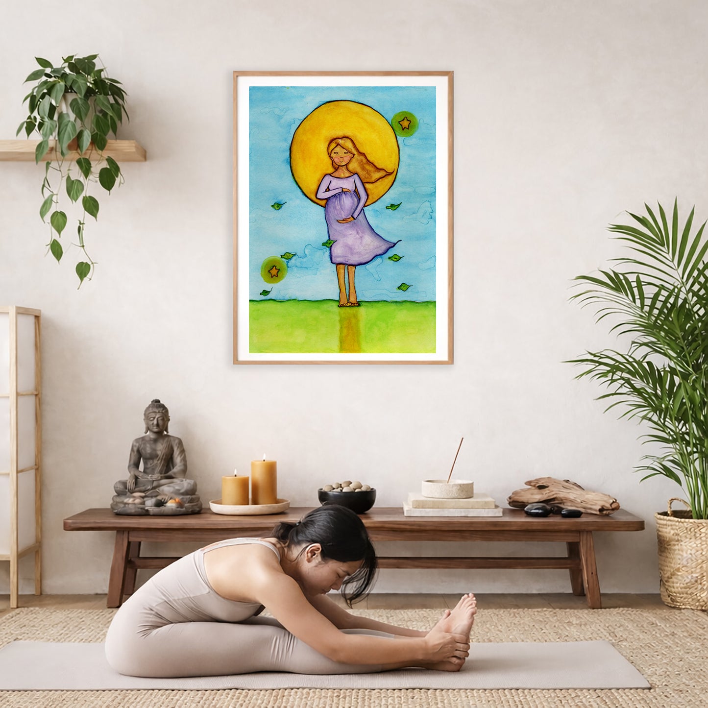Woman standing in meditation under a glowing sun with blue sky background, calming watercolor spiritual illustration. The poster is framed and is in the center of the living room wall. A woman is doing a sitting forward bend on her yoga mat. There is a coffee table below the poster with burning candles, incense, a Buddha statue and a big piece of driftwood.