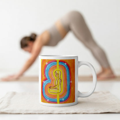 Woman surrounded by radiant multi-colored aura, representing energy, emotion and spiritual awareness, vibrant mindfulness artwork on a coffee mug.  The mug is in front of a woman doing the yoga posture downward facing dog.