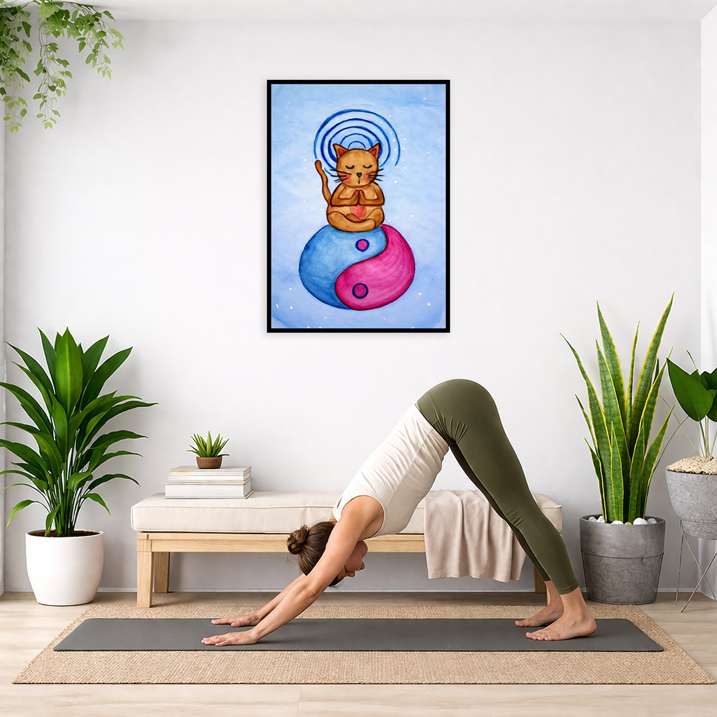 Brown cat meditating on a yin yang symbol with its crown chakra glowing framed poster.  This is a print of the original hand-painted watercolor by Brazilian artist Thaís Suizo.  The poster is in the center of the living room wall. Below the poster a woman is doing the yoga posture downward facing dog on a yoga mat.
