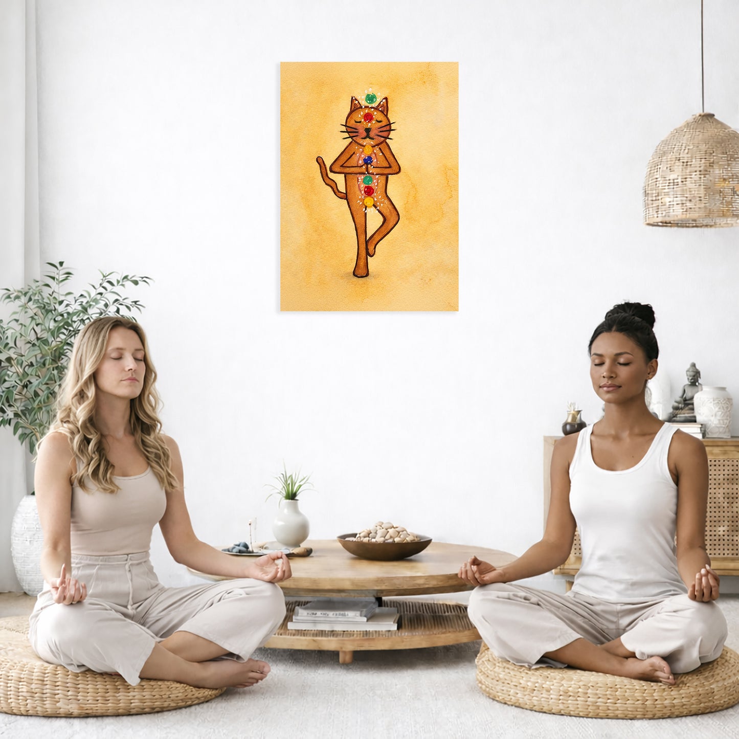 Two women meditating in a room with a painting of a chakra cat on the wall.