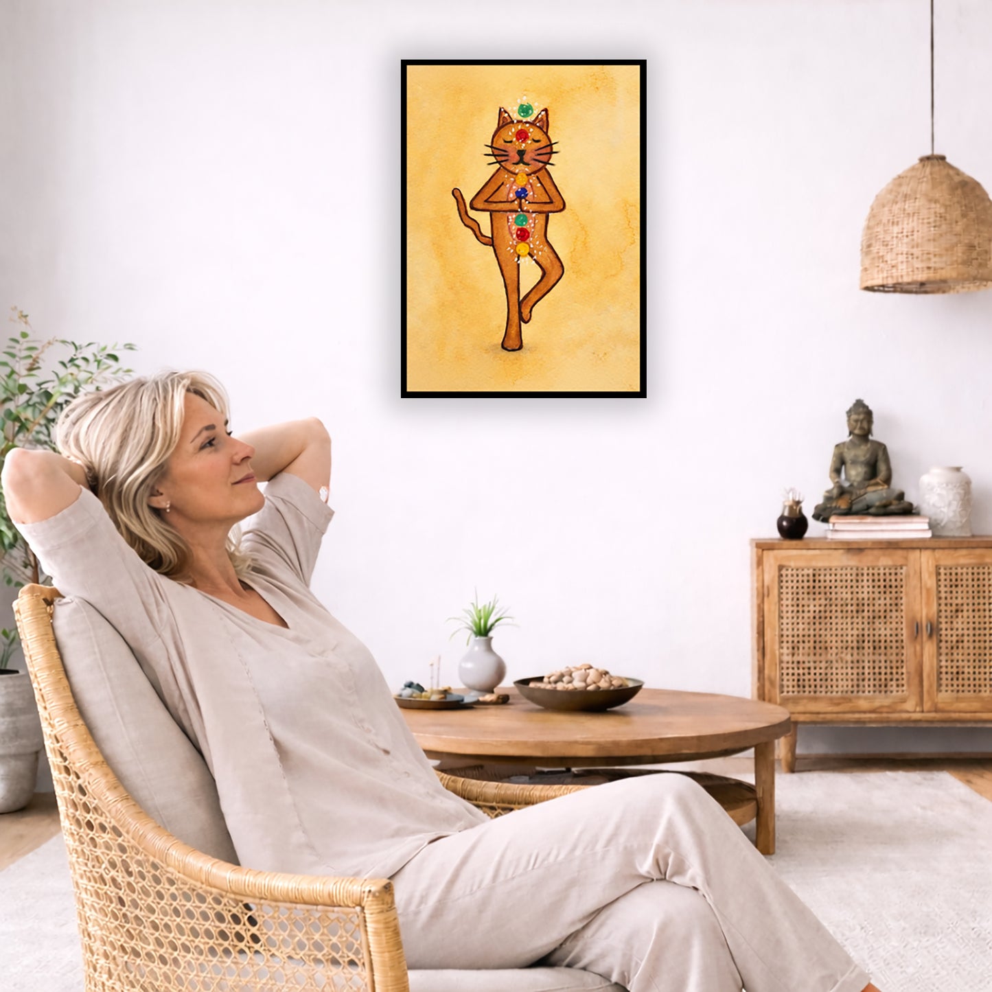 A brown cat standing in meditation with its chakras glowing framed poster.   This is a print of the original hand-painted watercolor by Brazilian artist Thaís Suizo.  The poster is in the center of the living room wall. To the left a woman is relaxing in her chair with her hands behind her head. There is a small coffee table beside her with a bowl of walnuts, incense and a small green plant. On the right side of the room is a cabinet with a Buddha statue, books and an urn on it. To the left is a green floor