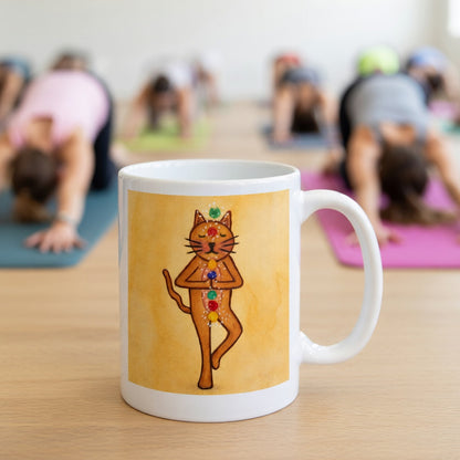 Brown cat standing in a meditation pose with glowing chakras along its body on a yellow background meditation mug.  The mug is in front of a yoga class doing the downward facing dog posture.