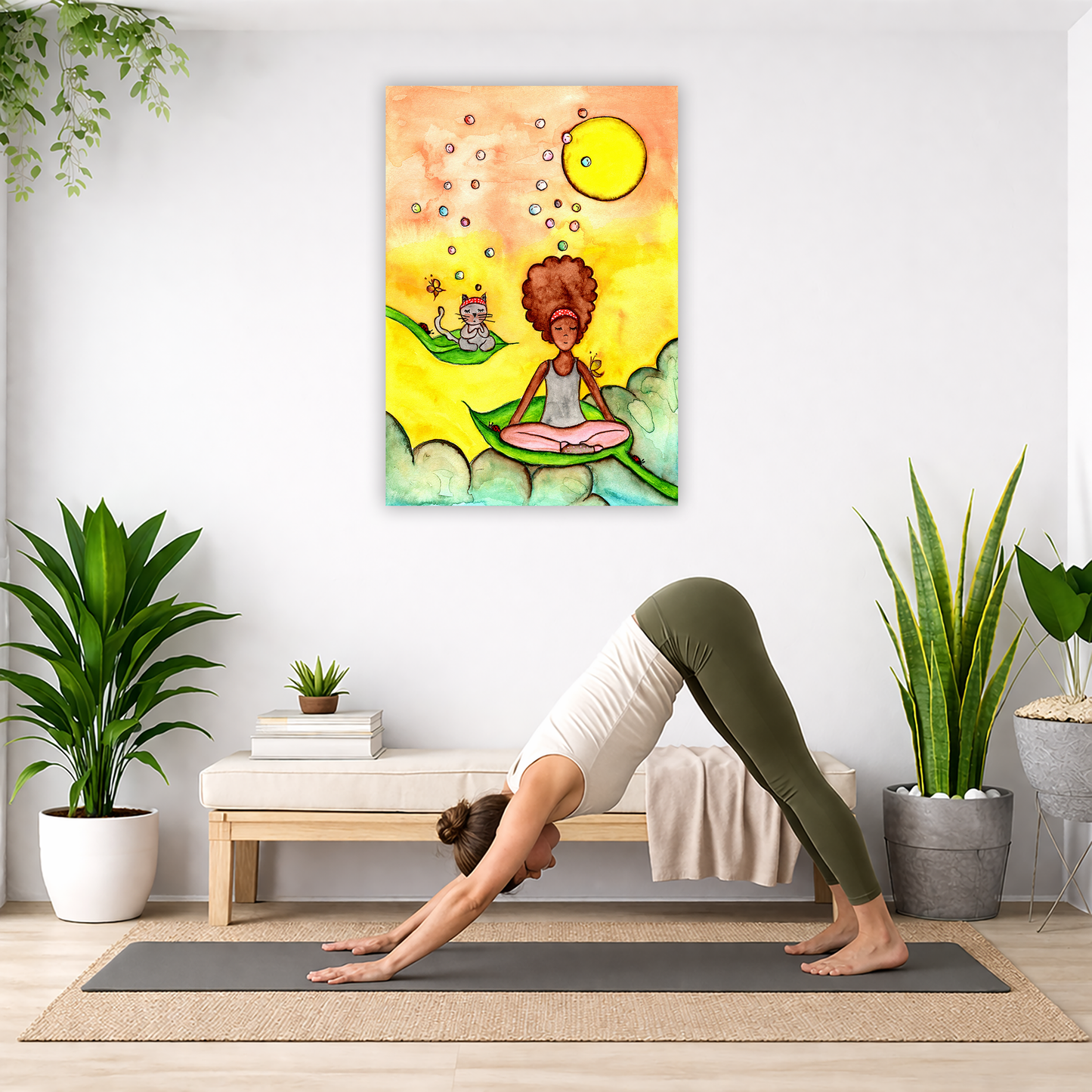 Canvas of a woman and her cat meditating while sitting on leaves. The background is bright yellow. The canvas is in the center of the living room wall. Below the poster a woman is doing the yoga posture downward facing dog on a yoga mat.