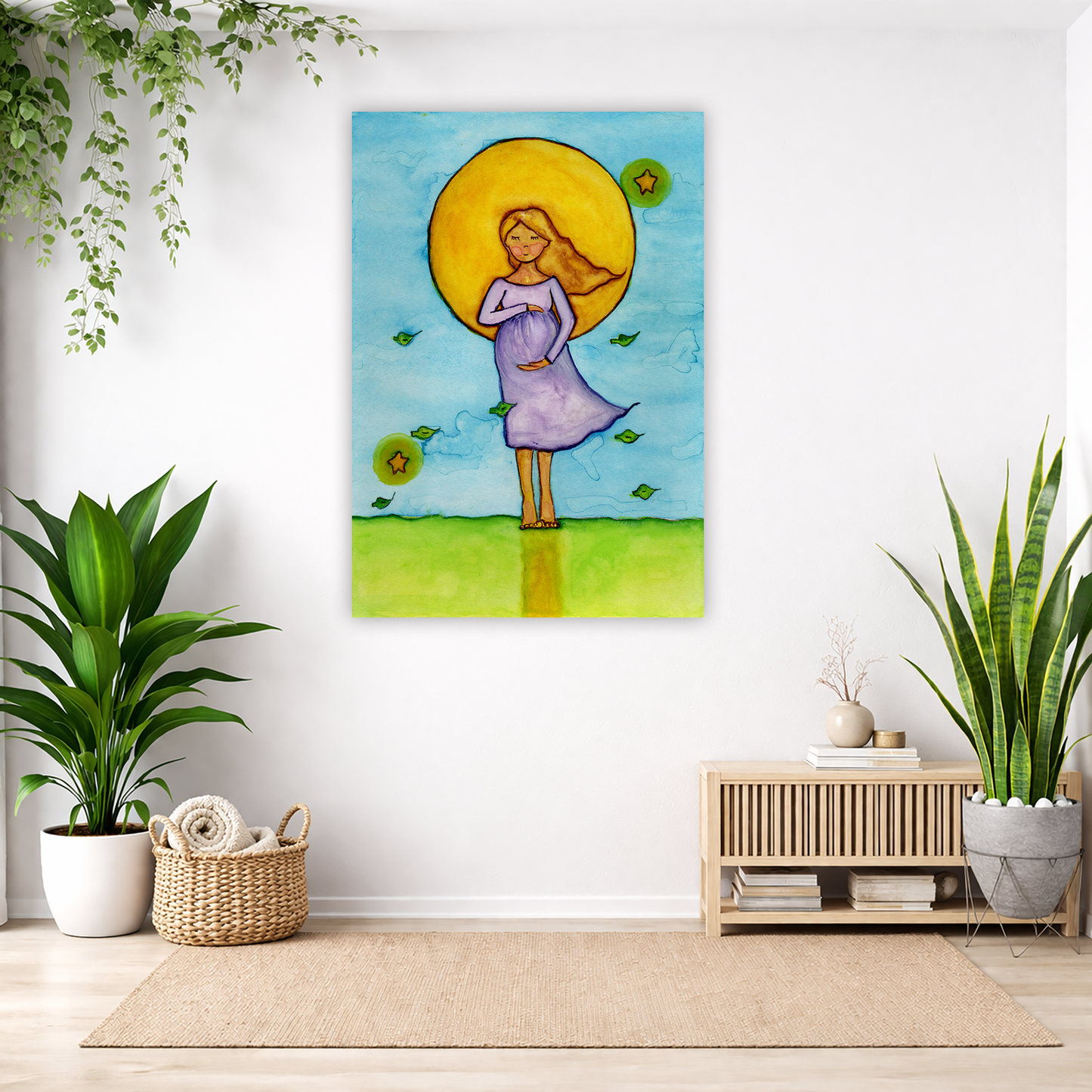 A woman standing in meditation under a bright yellow sun with a blue sky background, canvas watercolor print.  The canvas is in the center of the living room wall. Below the poster to the left is a basket of material and a green floor plant. There is also a green hanging plant. To the right is a small table with books, a candle and a vase with dry flora. There is also a large green floor plant.