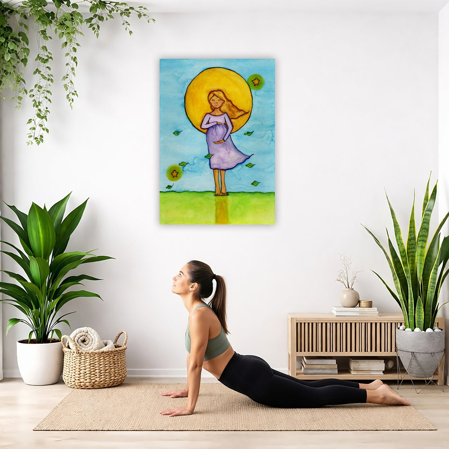 A woman standing in meditation under a bright yellow sun with a blue sky background, canvas watercolor print.  The canvas is in the center of the living room wall. Below the poster a woman is doing the yoga posture downward facing dog on a yoga mat.