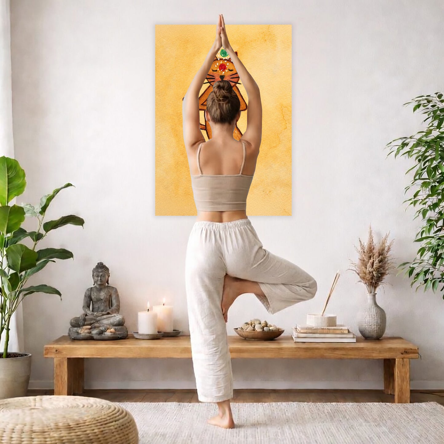 A poster with a brown cat in standing meditation pose with glowing chakras aligned along the body. The poster is framed hanging on a living room wall. A woman is doing the yoga tree pose (Vrksasana) facing the poster. There is a coffee table in front of her with candles and a Buddha statue. There are green potted plants on each side of the room.
