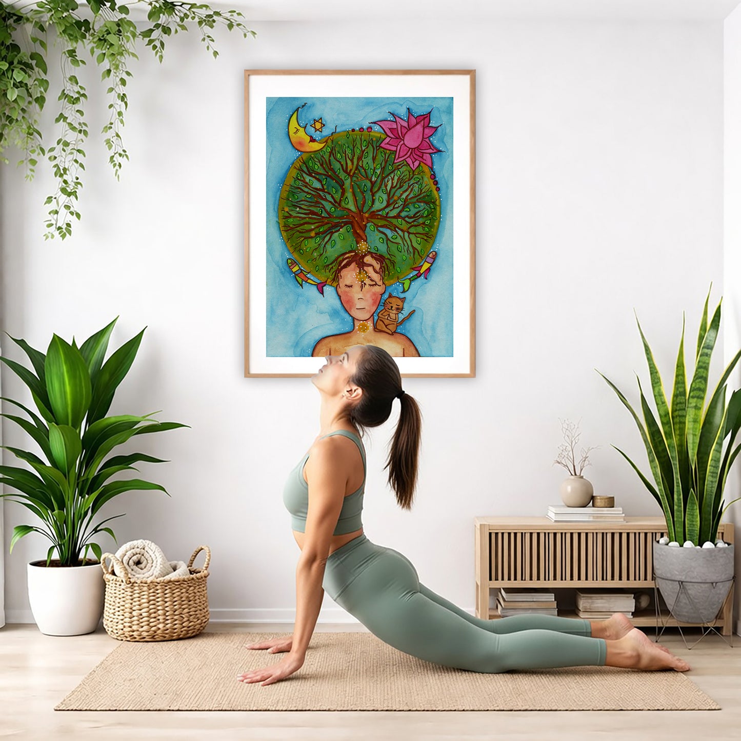 Poster of the crown chakra of a woman opening up like the tree of life. A cat is on her shoulder.  The poster is in the center of the living room wall. Below the poster a woman is doing the yoga posture downward facing dog on a yoga mat.