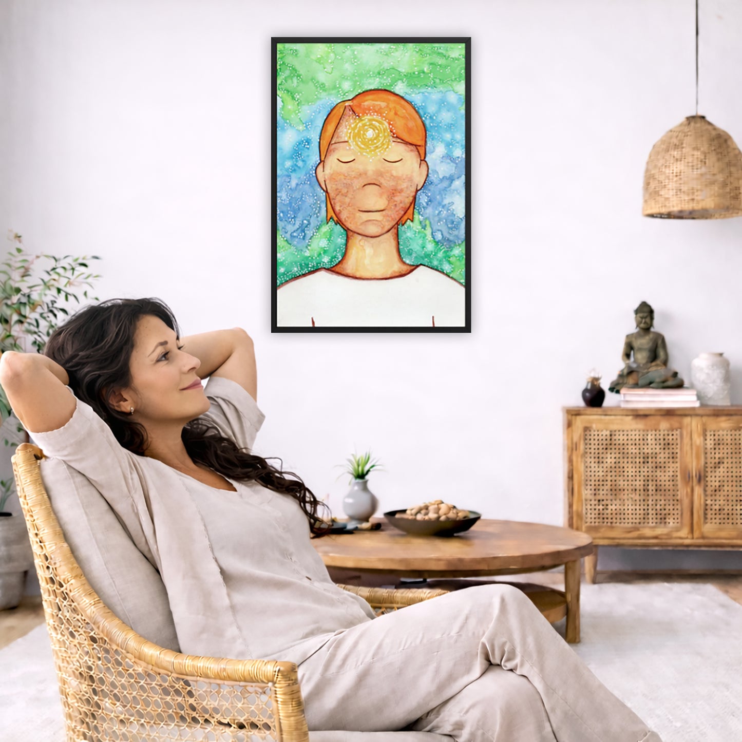 Framed poster of a man with a glowing brow chakra.  The poster is in the center of the living room wall. To the left a woman is relaxing in her chair with her hands behind her head. There is a small coffee table beside her with a bowl of walnuts, incense and a small green plant. On the right side of the room is a cabinet with a Buddha statue, books and an urn on it. To the left is a green floor plant.
