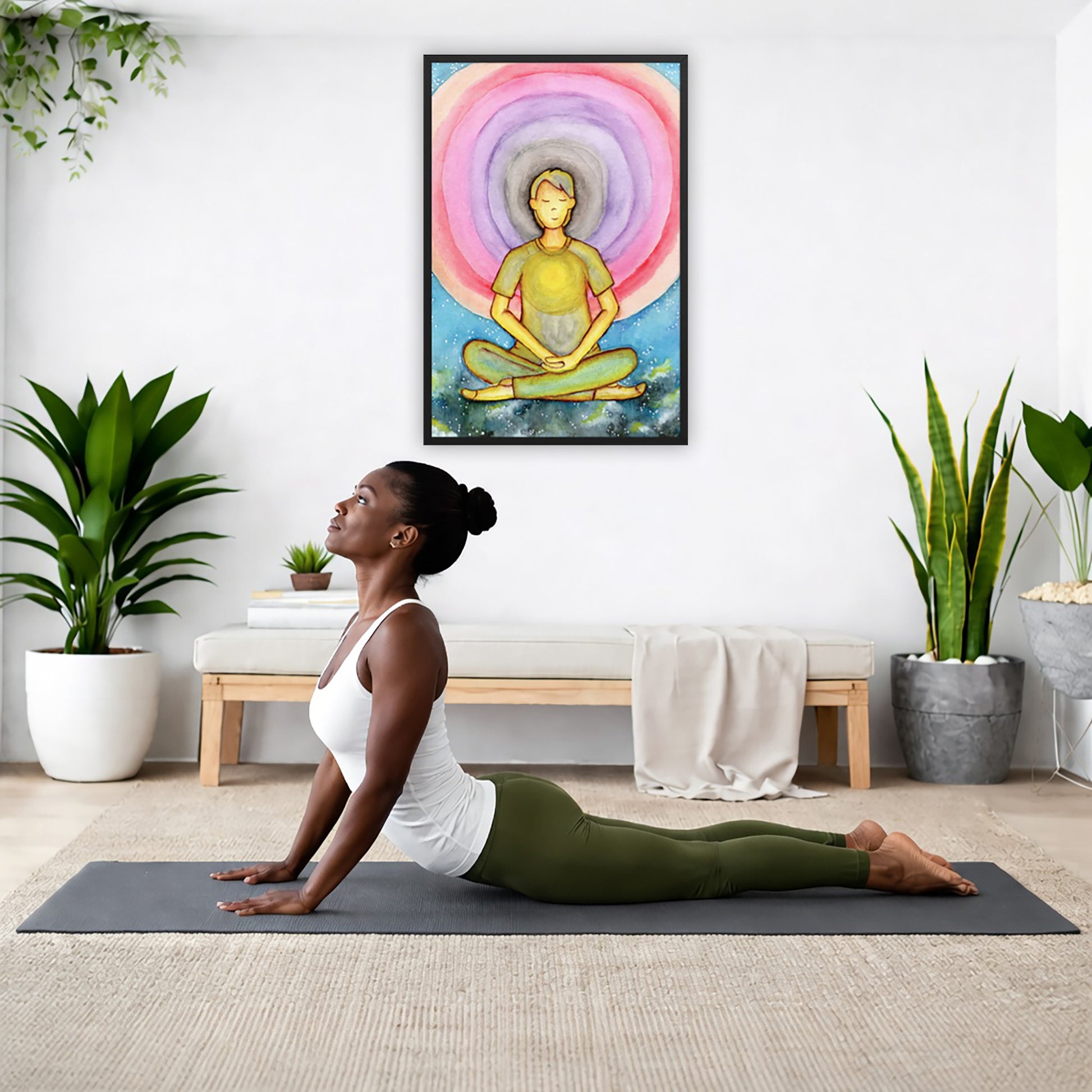 Framed poster of a man's heart chakra glowing and the colorful aura energy surrounding him.  The poster is hanging on the wall. A woman on her yoga mat is doing the cobra pose in front of the poster. There is a potted plant and a hanging plant on the left side. A padded bench with material draped over it is behind her. On the right side are two potted plants.
