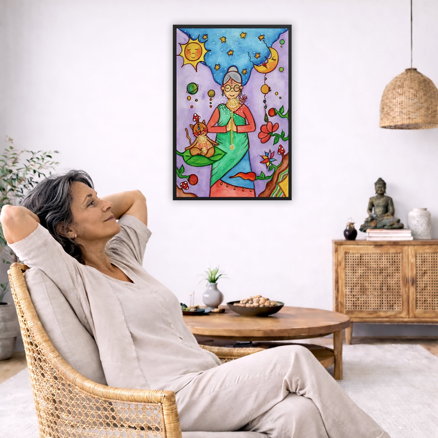 Framed poster of woman in standing prayer meditation with glowing throat chakra under sun and moon. Her cat is meditating beside her.  The poster is in the center of the living room wall. To the left a man is relaxing in her chair with his hands behind his head. There is a small coffee table beside him with a bowl of walnuts, incense and a small green plant. On the right side of the room is a cabinet with a Buddha statue, books and an urn on it. To the left is a green floor plant.
