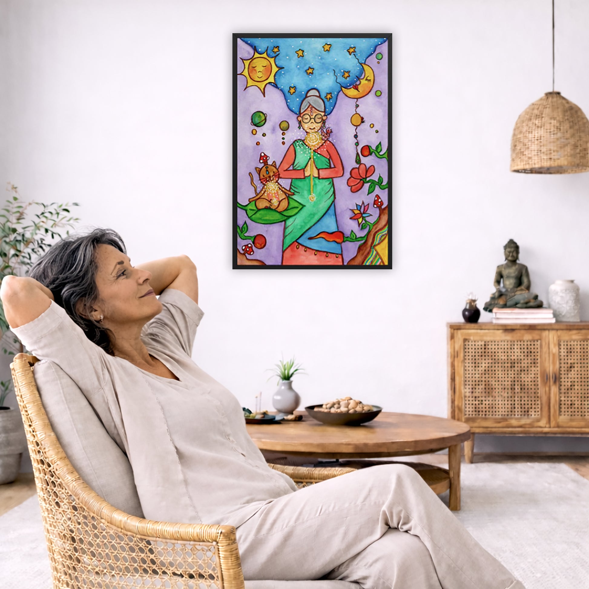 Framed poster of woman in standing prayer meditation with glowing throat chakra under sun and moon. Her cat is meditating beside her.  The poster is in the center of the living room wall. To the left a man is relaxing in her chair with his hands behind his head. There is a small coffee table beside him with a bowl of walnuts, incense and a small green plant. On the right side of the room is a cabinet with a Buddha statue, books and an urn on it. To the left is a green floor plant.
