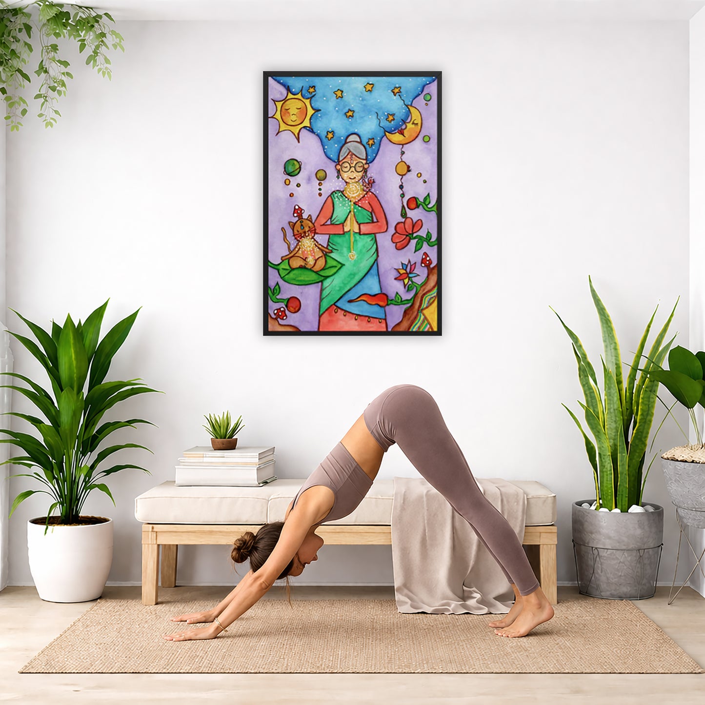 Framed poster of woman in standing prayer meditation with glowing throat chakra under sun and moon. Her cat is meditating beside her.  The poster is in the center of the living room wall. Below the poster a woman is doing the yoga posture downward facing dog on a yoga mat.