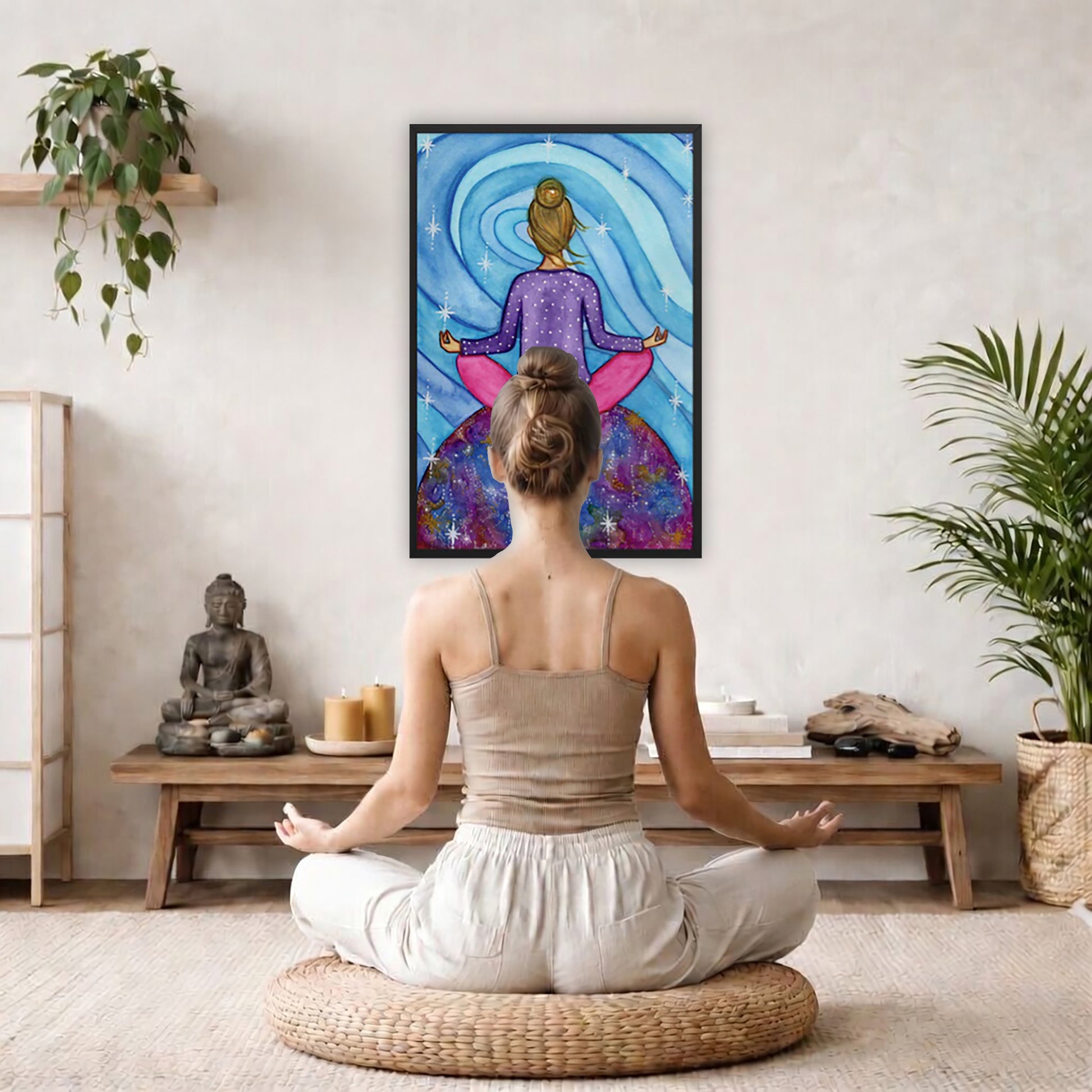 Framed poster of a woman meditating on top of the world with her root chakra glowing.  The poster is framed hanging on a living room wall. A woman is mediating facing the poster. There is a coffee table in front of her with burning candles and a Buddha statue. There are green potted plants on each side of the room.
