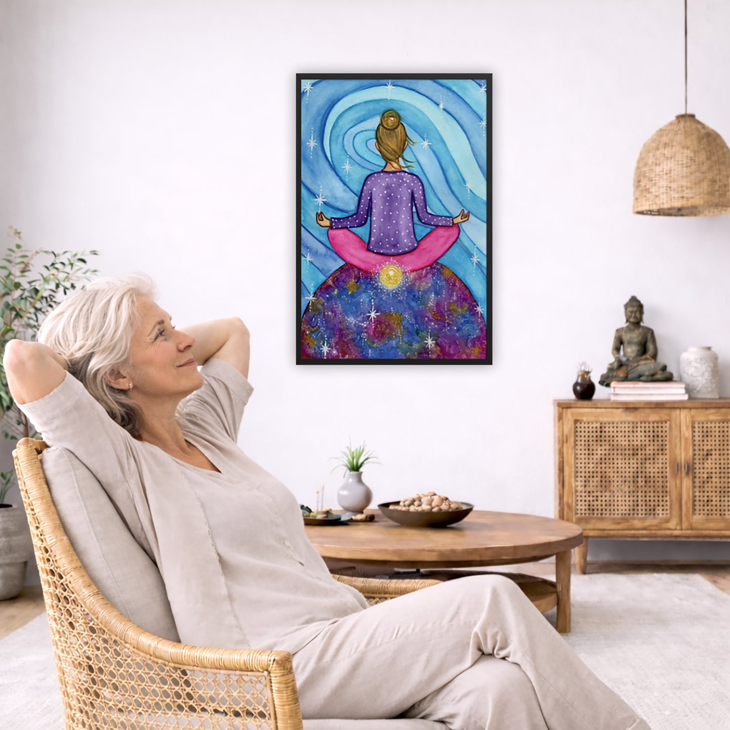 Framed poster of a woman meditating on top of the world with her root chakra glowing.  The poster is in the center of the living room wall. To the left a woman is relaxing in her chair with her hands behind her head. There is a small coffee table beside her with a bowl of walnuts, incense and a small green plant. On the right side of the room is a cabinet with a Buddha statue, books and an urn on it. To the left is a green floor plant.
