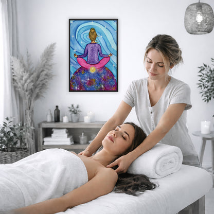 Framed poster of a woman meditating on top of the world with her root chakra glowing.  The poster is on the wall of the office of a massage therapist. The therapist is giving her female client a massage. The client is lying face up on a massage table wearing a white towel. To the left is a window, floor plant and large vase of dry flora. A shelf is underneath the poster with candles burning. There is a candle burning on a small table and a hanging lamp with a wicker shade on the right side.
