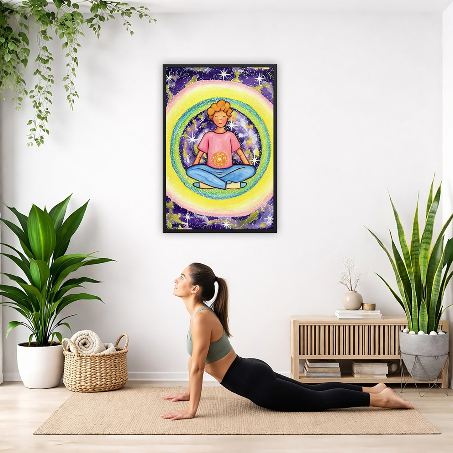 Framed poster of a young man meditating with his solar plexus glowing. He is basking in his colorful aura.  The poster is hanging on the wall. A woman on her yoga mat is doing the cobra pose in front of the poster. There is a potted plant and a hanging plant on the left side. A padded bench with material draped over it is behind her. On the right side are two potted plants.
