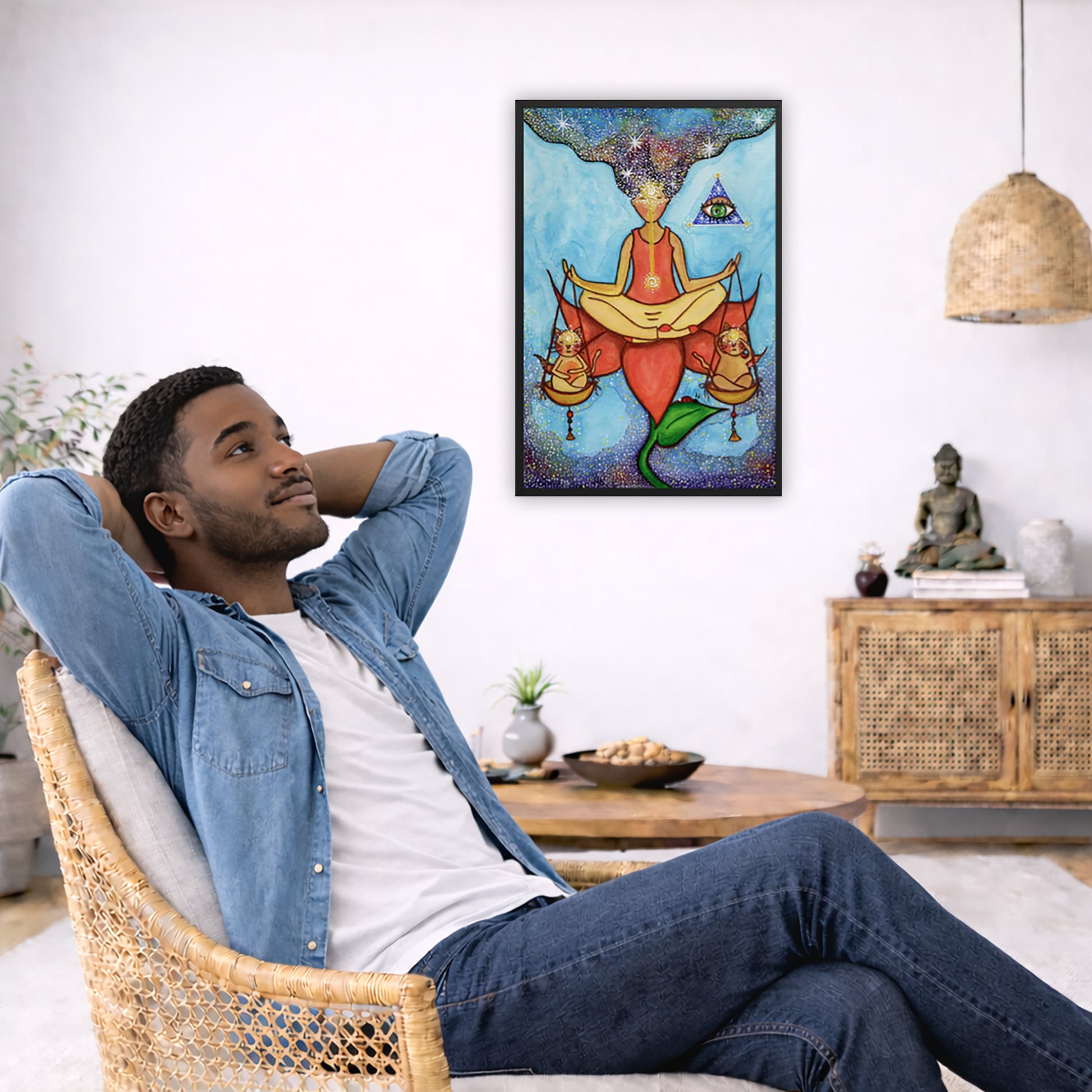 Framed poster of a woman sitting on a lotus with a glowing brow chakra holding a large set of scales.  The poster is in the center of the living room wall. To the left a man is relaxing in her chair with his hands behind his head. There is a small coffee table beside him with a bowl of walnuts, incense and a small green plant. On the right side of the room is a cabinet with a Buddha statue, books and an urn on it. To the left is a green floor plant.
