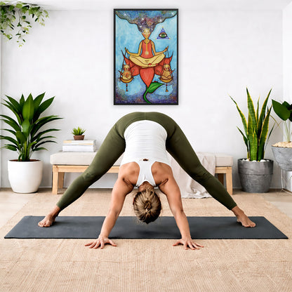 Framed poster of a woman sitting on a lotus with a glowing brow chakra holding a large set of scales.  The poster is in the center of the living room wall. A woman is doing a forward bend on her yoga mat. There is a padded bench below the poster with some books and a small potted plant on it. To the right and left are potted plants.
