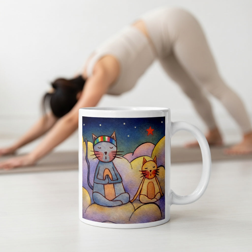 Two cats meditating on a cloud under the night sky mindfulness mug. The mug is in front of a woman doing the yoga posture downward facing dog.