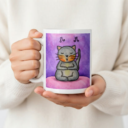 A gray cat is listening to music and chanting on a pink background with notes floating in the air mug.  The hands of a person wearing a white sweater are holding the mug up to display the design.