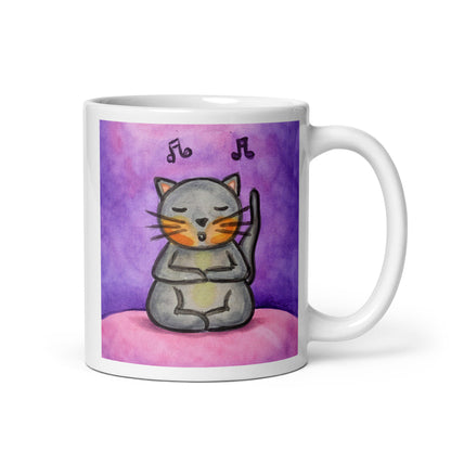 A gray cat is listening to music and chanting on a pink background with notes floating in the air mug. This illustration of a cat meditating is on both sides of the mug. In this image the handle of the mug is on the right side.