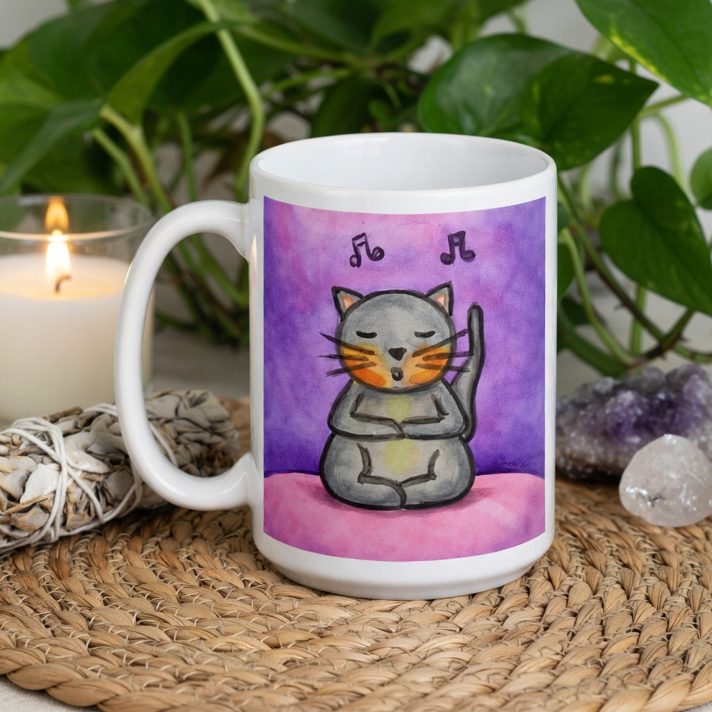 A gray cat is listening to music and chanting on a pink background with notes floating in the air mug.  The mug is sitting on a wicker mat with crystals, a burning candle and green plant behind it.