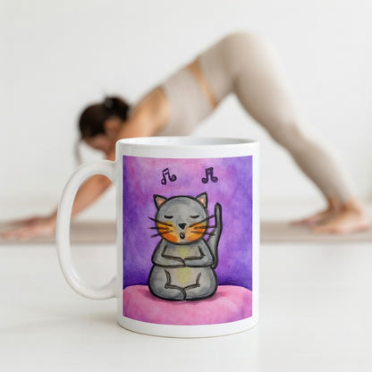 A gray cat is listening to music and chanting on a pink background with notes floating in the air mug. The mug is in front of a woman doing the yoga posture downward facing dog.