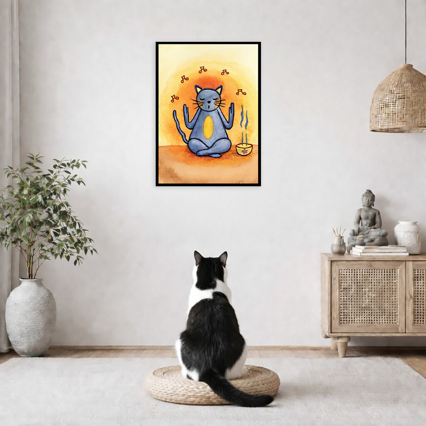 Gray cat chants with incense burning framed poster.  This is a print of the original hand-painted watercolor by Brazilian artist Thaís Suizo.  The poster is in the center of the living room wall. A black and white cat is staring at the poster. There is a potted plant on the left side and a cabinet with a Buddha statue on it on the right side. 
