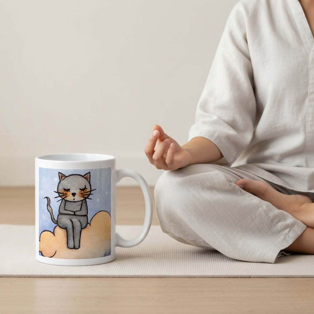 Gray cat Meditating on an orange cloud mindfulness coffee mug.  The mug is sitting on a white mat. A woman is meditating in the background.