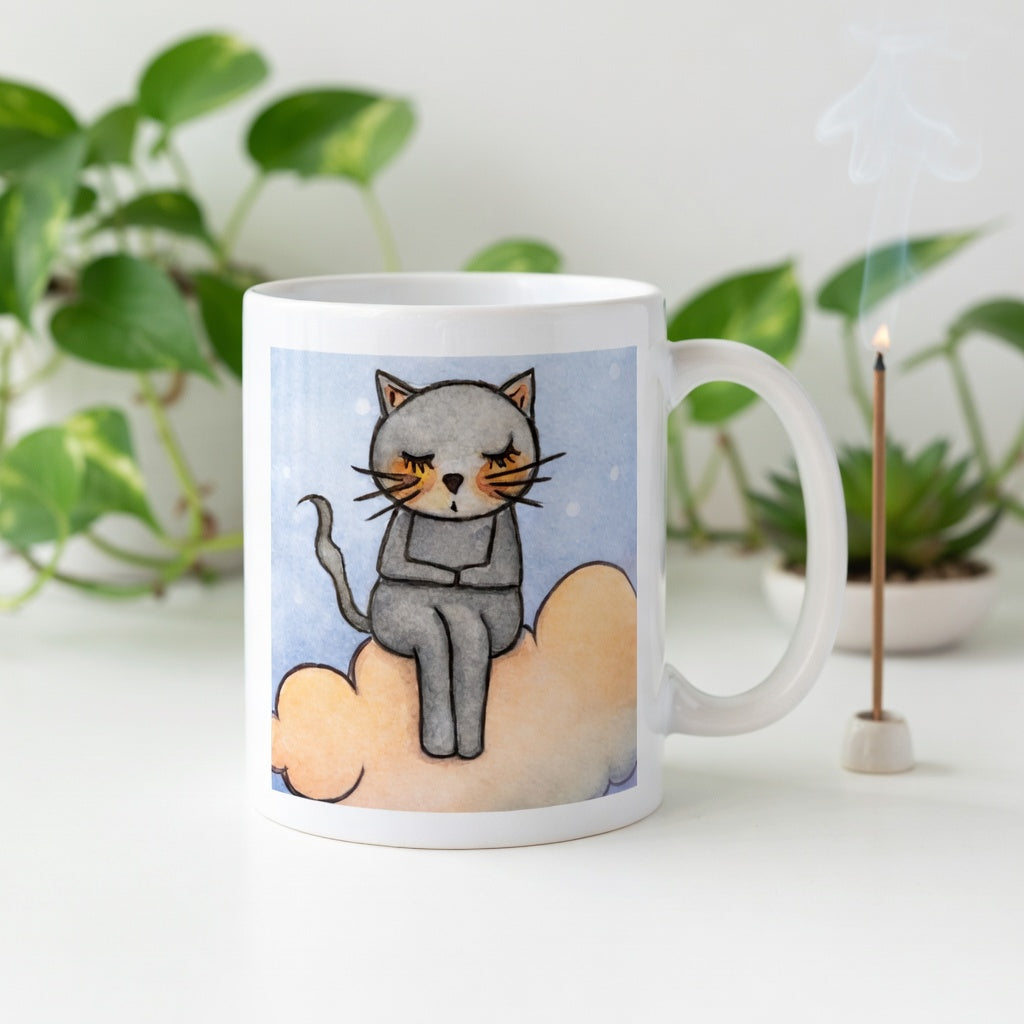 Gray cat Meditating on an orange cloud mindfulness coffee mug.  Incense is burning behind the mug. There is a green potted plant in the background.
