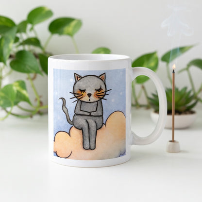 Gray cat Meditating on an orange cloud mindfulness coffee mug.  Incense is burning behind the mug. There is a green potted plant in the background.
