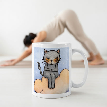 Gray cat Meditating on an orange cloud mindfulness coffee mug.  The mug is in front of a woman doing the yoga posture downward facing dog.