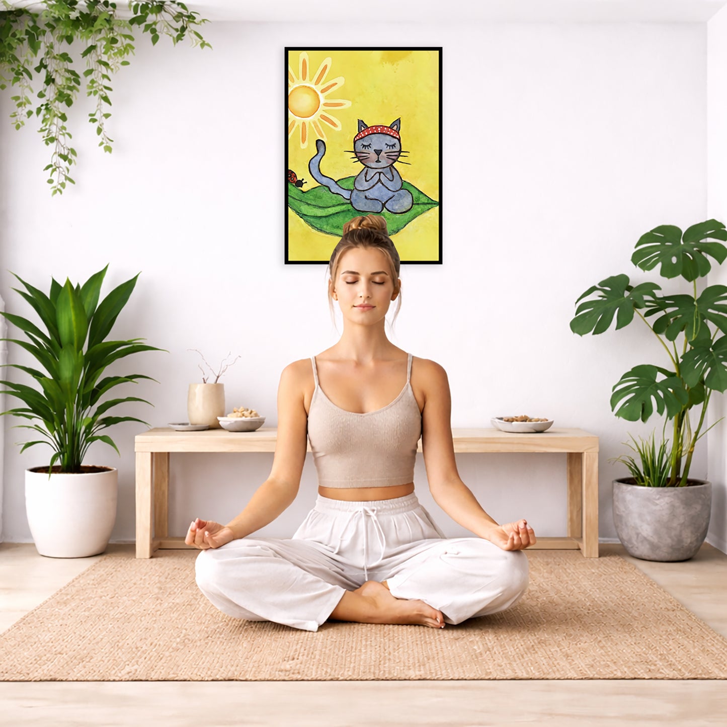 Gray cat meditating on a leaf under a sunny sky framed poster. This is a print of the original hand-painted watercolor by Brazilian artist Thaís Suizo.  The poster is framed hanging on a living room wall. A woman is mediating facing the poster. There is a coffee table in front of her with burning candles and a Buddha statue. There are green potted plants on each side of the room.
