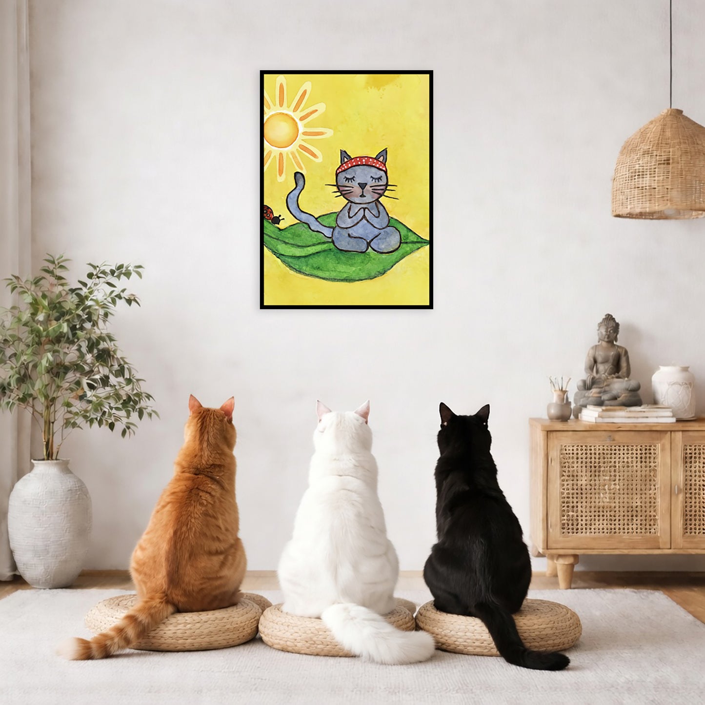 Gray cat meditating on a leaf under a sunny sky framed poster. This is a print of the original hand-painted watercolor by Brazilian artist Thaís Suizo.  Three friends are sitting on wicker pillows meditating in a living room. The poster framed is on the wall behind them. The table behind them has a Buddha statue and a lit candle. There is a white curtain to the left and a hanging lamp and a potted green plant on the right.