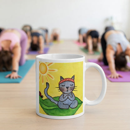 Gray cat meditating peacefully on a leaf in the bright sunlight meditation mug.  The mug is in front of a yoga class doing the downward facing dog posture.