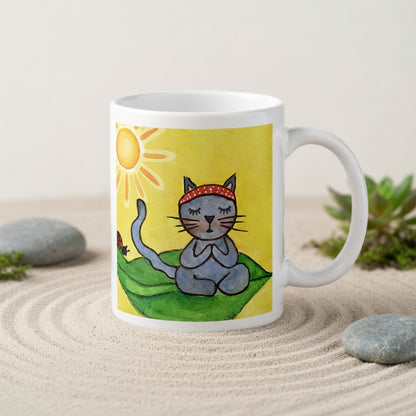 Gray cat meditating peacefully on a leaf in the bright sunlight meditation mug.  The mug is in a beautifully raked zen garden with bushes and plants behind it.