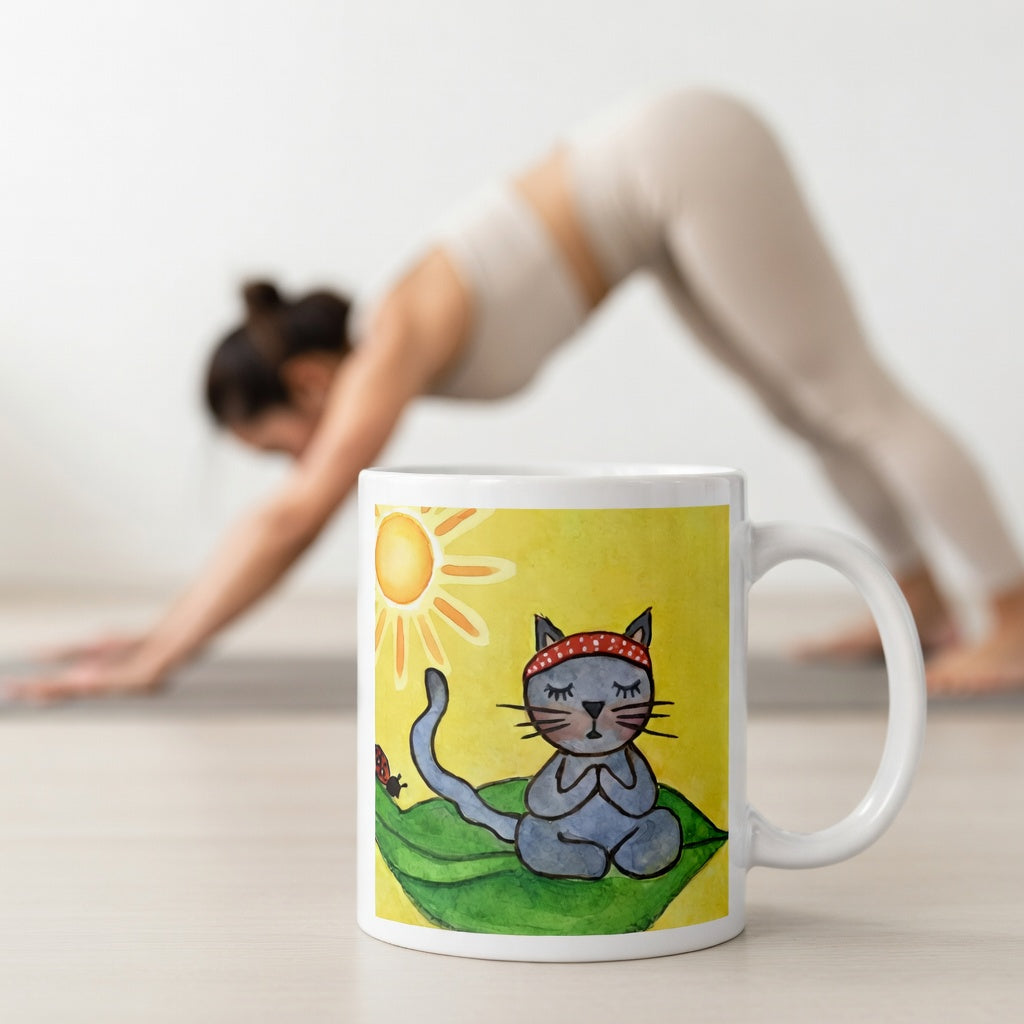 Gray cat meditating peacefully on a leaf in the bright sunlight meditation mug.  The mug is in front of a woman doing the yoga posture downward facing dog.