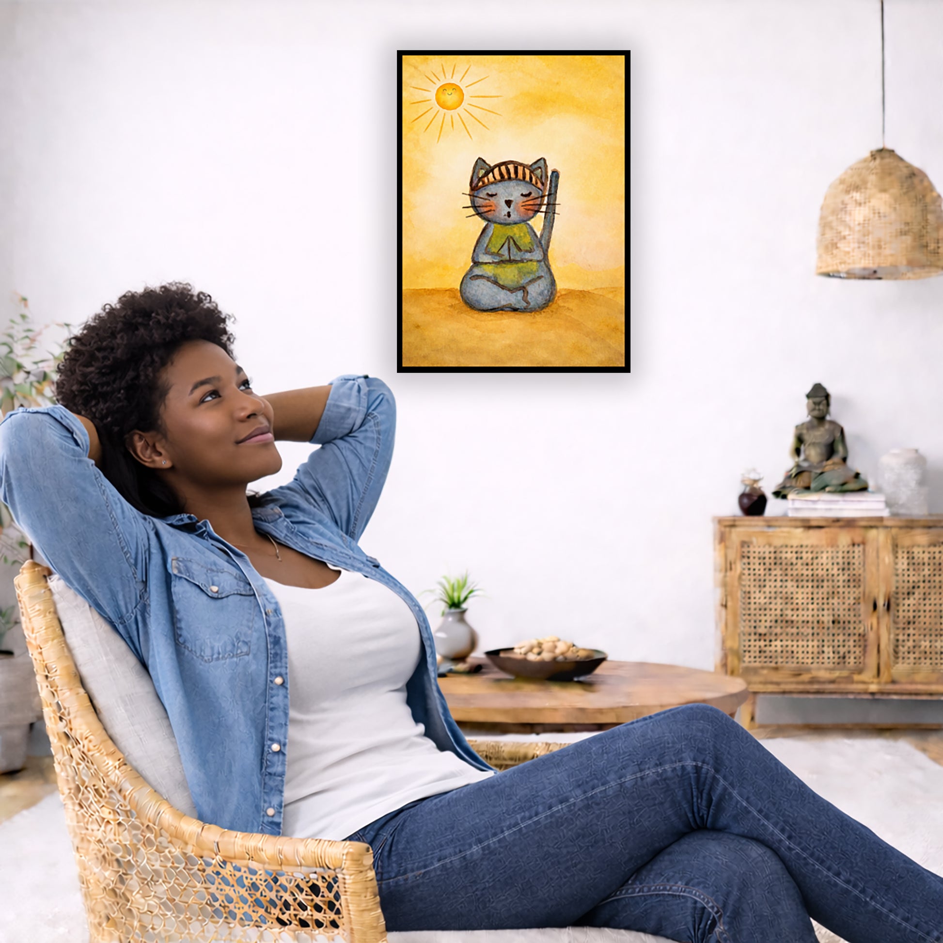 A gray cat meditating on a sunny day framed poster.  This is a print of the original hand-painted watercolor by Brazilian artist Thaís Suizo. The poster is in the center of the living room wall. To the left a woman is relaxing in her chair with her hands behind her head. There is a small coffee table beside her with a bowl of walnuts, incense and a small green plant. On the right side of the room is a cabinet with a Buddha statue, books and an urn on it. To the left is a green floor plant.