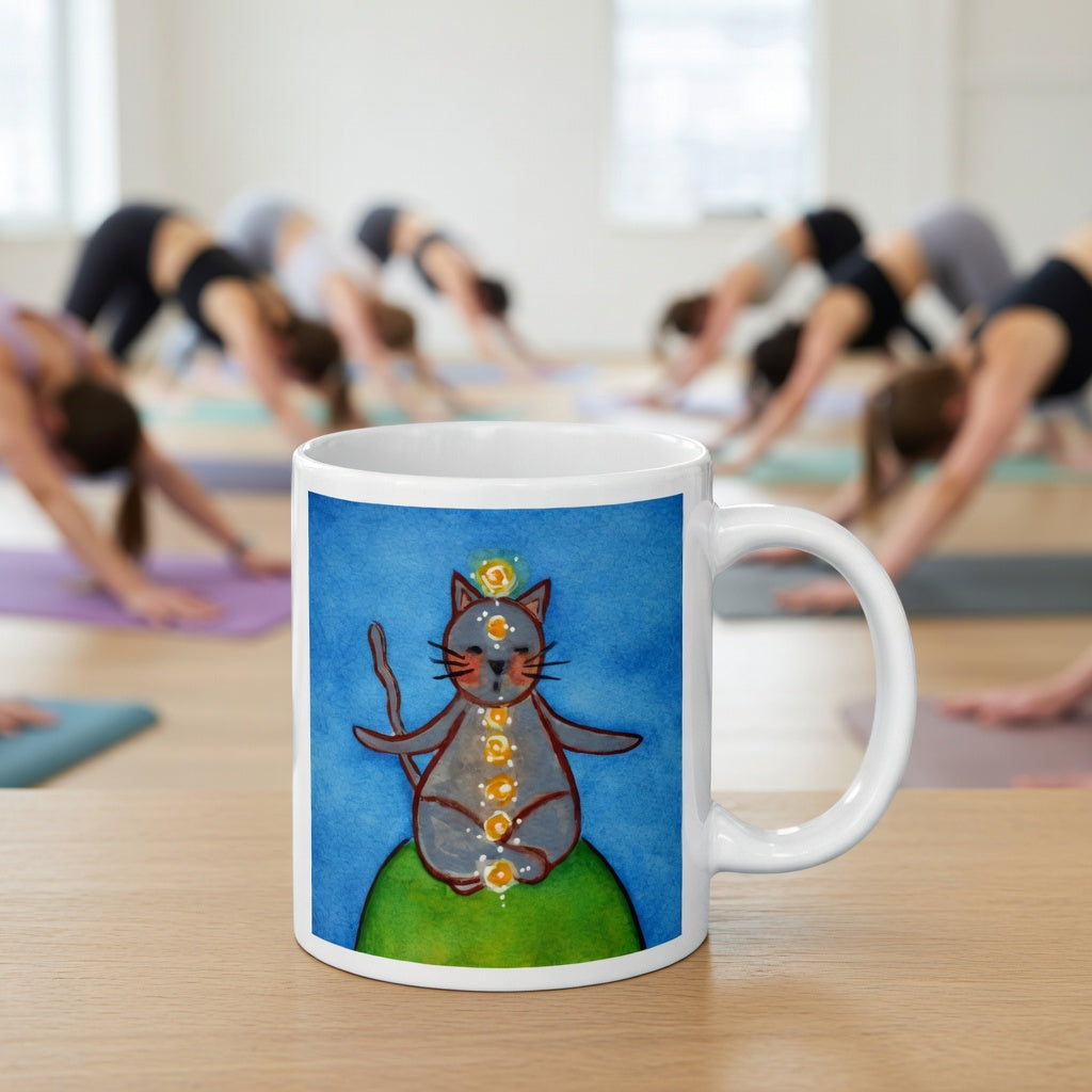 Gray cat meditating with glowing chakras on a deep blue calming background.  The mug is in front of a yoga class doing the downward facing dog posture.