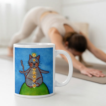 Gray cat meditating with glowing chakras on a deep blue calming background.  The mug is in front of a woman doing the yoga posture downward facing dog.