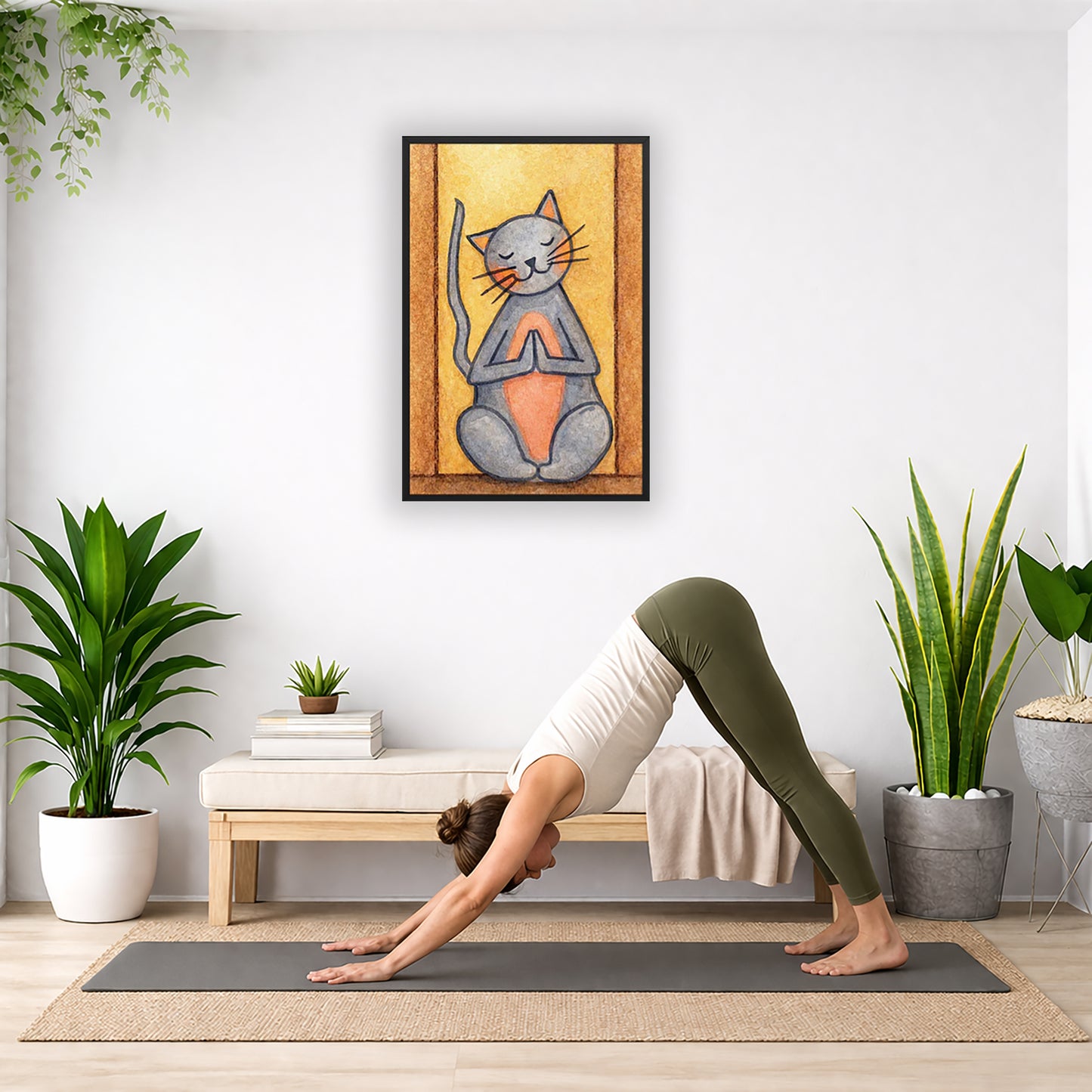 A gray cat with a pink belly is doing a standing meditation framed poster.  This is a print of the original hand-painted watercolor by Brazilian artist Thaís Suizo.   The poster is in the center of the living room wall. Below the poster a woman is doing the yoga posture downward facing dog on a yoga mat.
