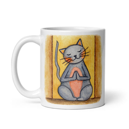 Gray cat with a pink belly on a yellow background is sitting in a peaceful meditation pose with praying paws in front of its chest. This illustration of a cat meditating is on both sides of the mug. In this image the handle of the mug is on the left side.