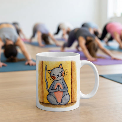 Gray cat with a pink belly on a yellow background is sitting in a peaceful meditation pose with praying paws in front of its chest.  The mug is in front of a yoga class doing the downward facing dog posture.