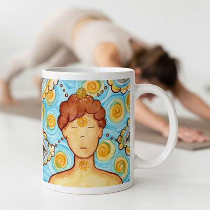 Man meditating with glowing throat, brow and crown chakras, symbolizing communication, intuition and spiritual connection, chakra artwork on a coffee mug.  The mug is in front of a woman doing the yoga posture downward facing dog.