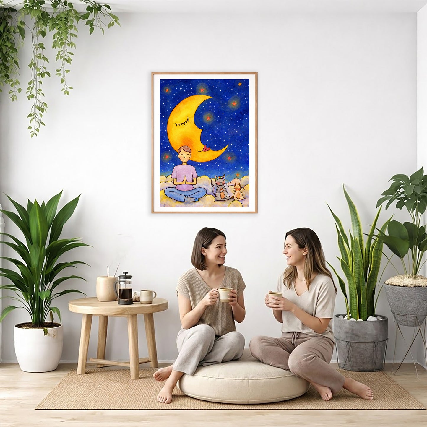Man with cats meditating under the moonlight on mindfulness poster.  The poster is framed and is in the center of the living room wall. Two women are sitting on a giant pillow having a coffee. Beside them is a small tray with a pot of coffee and incense. To the left is a green floor plant and a hanging green plant. To the right of them is a green floor plant.