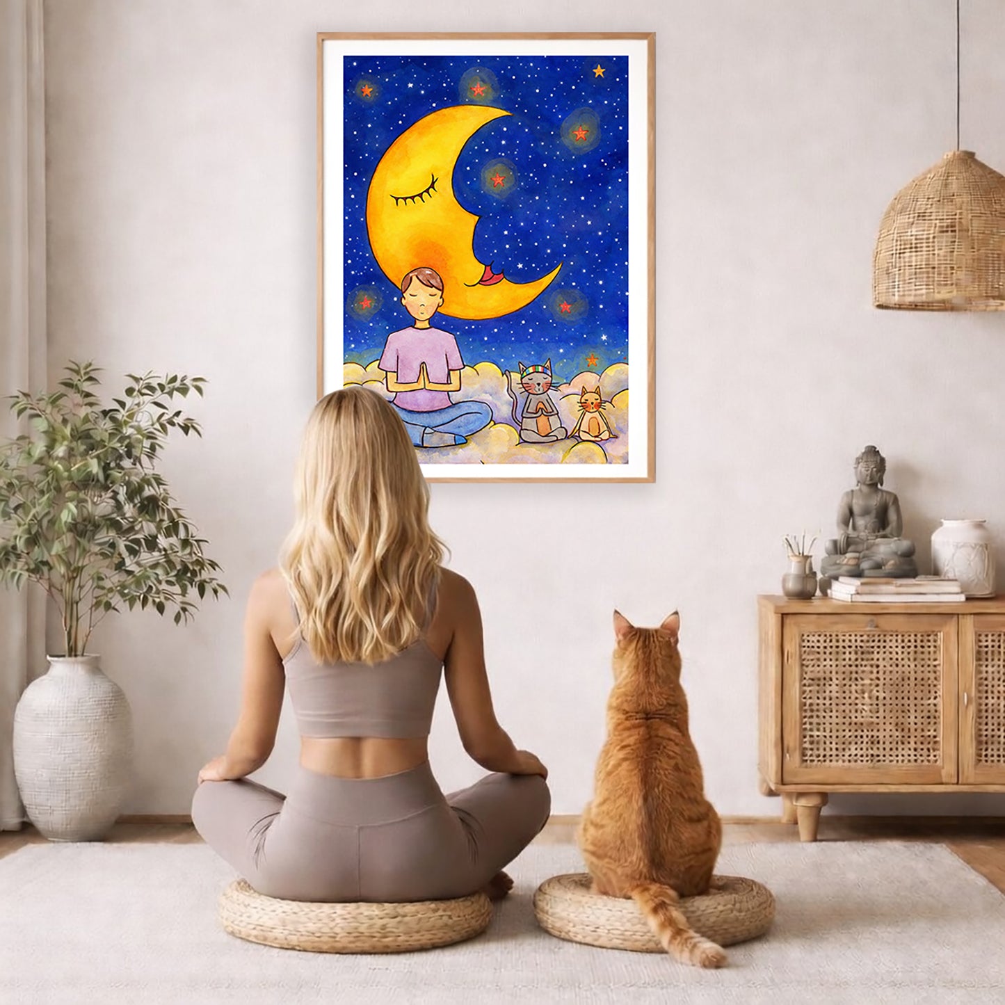 Man with cats meditating under the moonlight on mindfulness poster.  The poster framed is hanging on the wall. A woman and a cat are staring up at the poster. There is a potted plant on the left side and a cabinet with a Buddha statue, books and incense on the right side.
