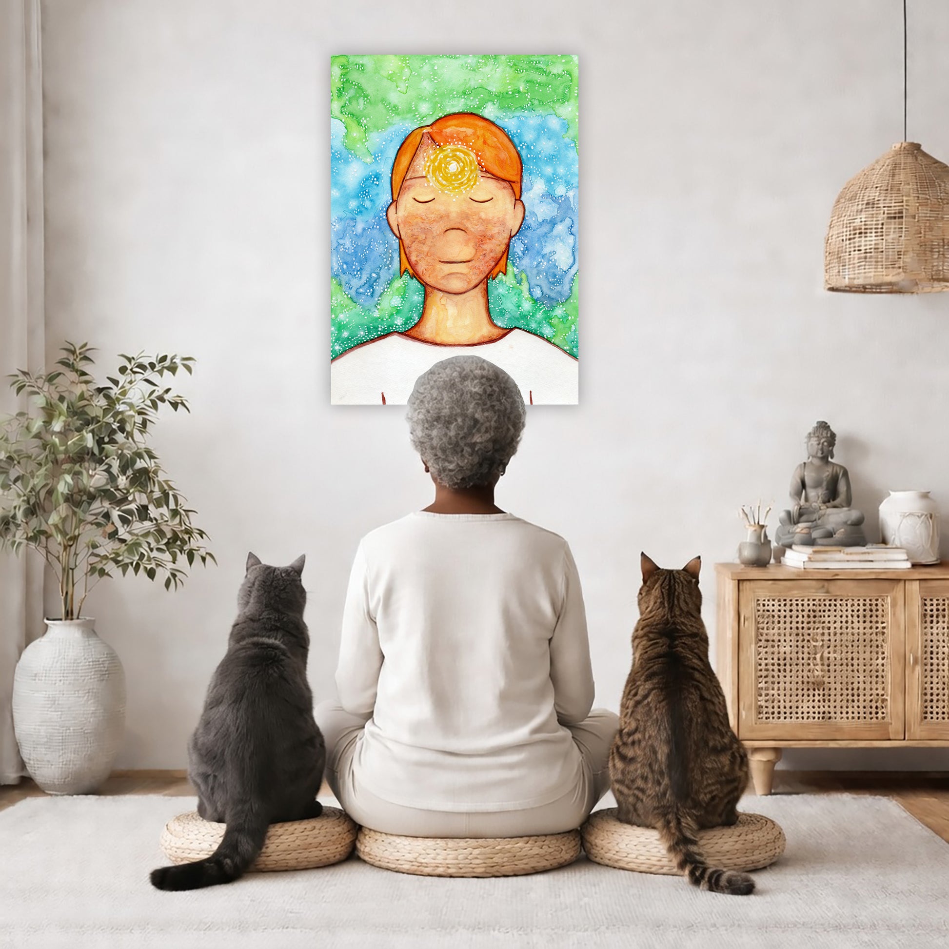 Man meditating with his brow chakra glowing canvas print.  The poster is in the center of the living room wall. A woman is meditating facing the poster with a white cat on her left side and a black cat on her right side. There is a potted plant on the left side and a cabinet with a Buddha statue on it on the right side. 
