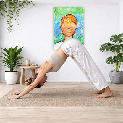 Man meditating with his brow chakra glowing canvas print.  The poster is in the center of the living room wall. Below the poster a woman is doing the yoga posture downward facing dog on a yoga mat.