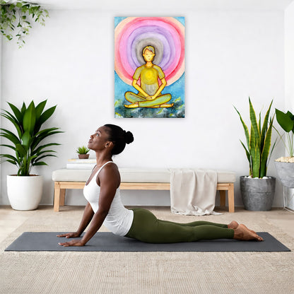 Canvas of a young man's heart chakra glowing and aura energy flowing around him. This is a print of the original hand-painted watercolor by Brazilian artist Thaís Suizo for the LET'S MEDITATE SERIES of mediation guides.  The poster is hanging on the wall. A woman on her yoga mat is doing the cobra pose in front of the poster. There is a potted plant and a hanging plant on the left side. A padded bench with material draped over it is behind her. On the right side are two potted plants.
